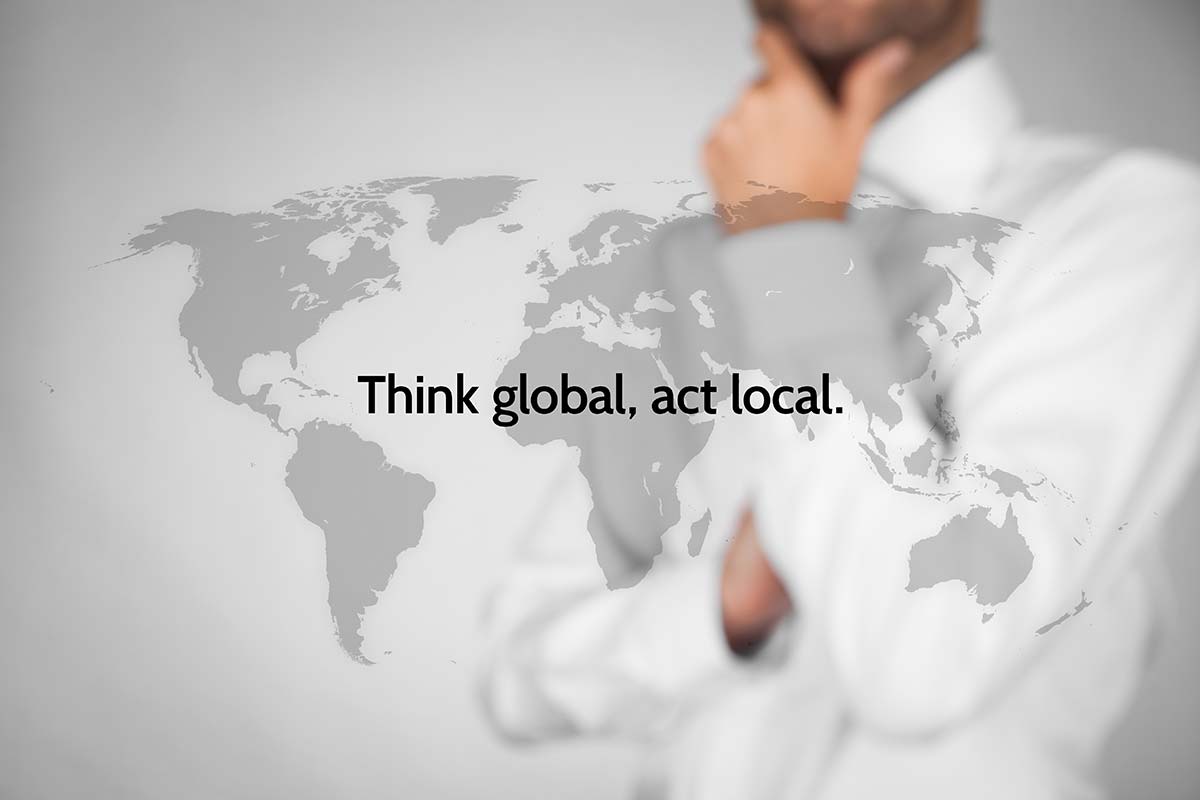 Professional pondering global strategies with 'Think global, act local' text overlay and world map background.