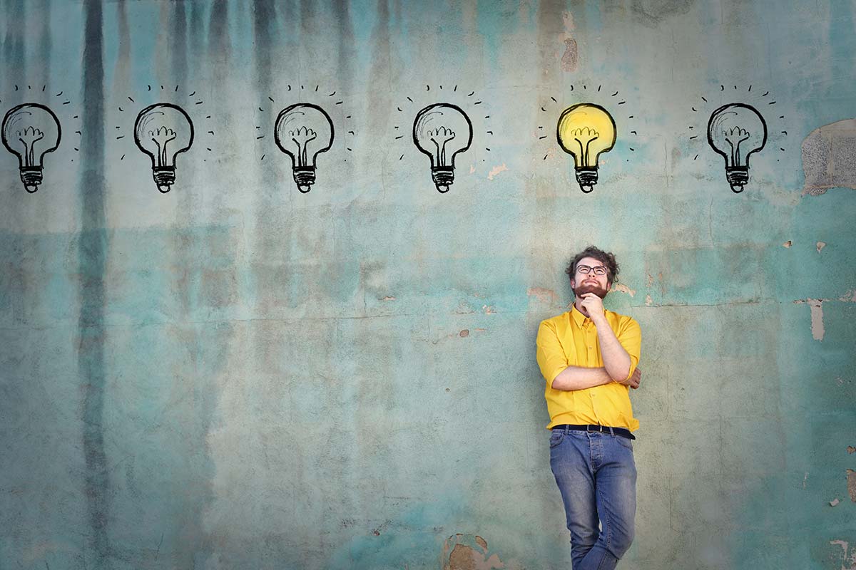 A man leaning against a wall. Above his head are lightbulbs representing that creative thinking leads to amazing ideas