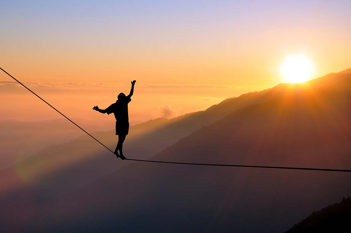 Tightrope walker balancing at sunset, symbolizing the balance between creativity and practicality in business.