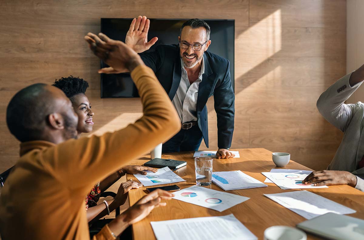 Team members high-fiving during a meeting, celebrating the momentum created by small wins in a collaborative work environment.