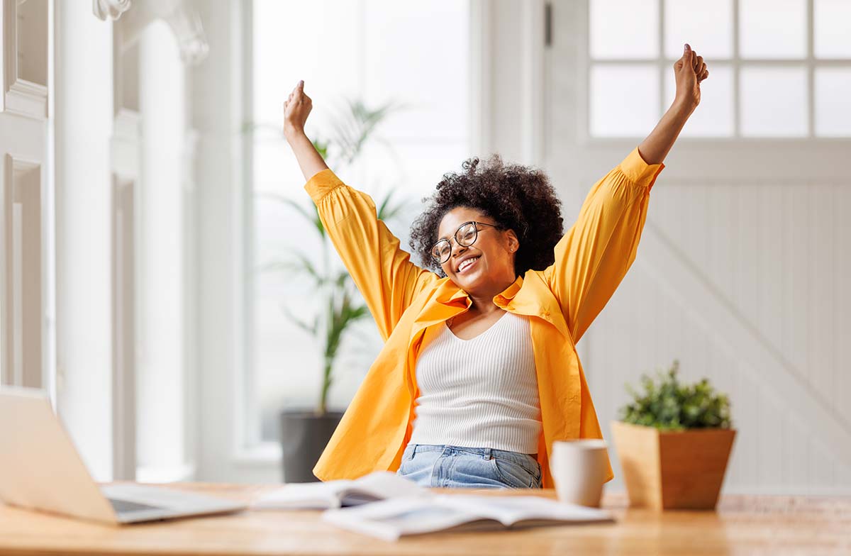 Happy woman stretching at her desk in a bright home office, embracing positivity.