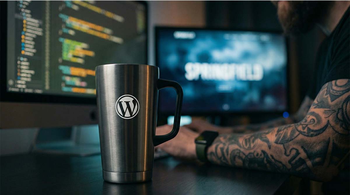 Developer working at a computer with WordPress logo on a coffee mug, symbolizing website development work