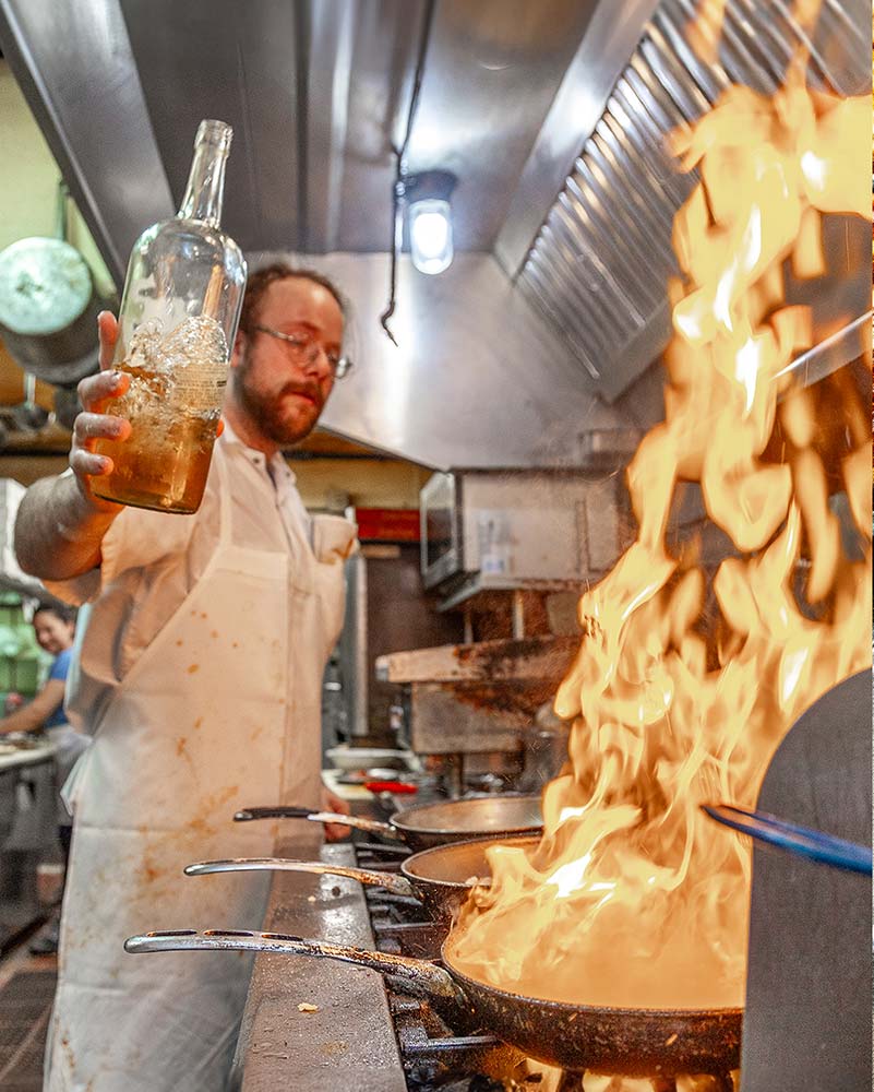 Chef deglazing a pan over open flame in Joe’s Cafe kitchen, Northampton MA