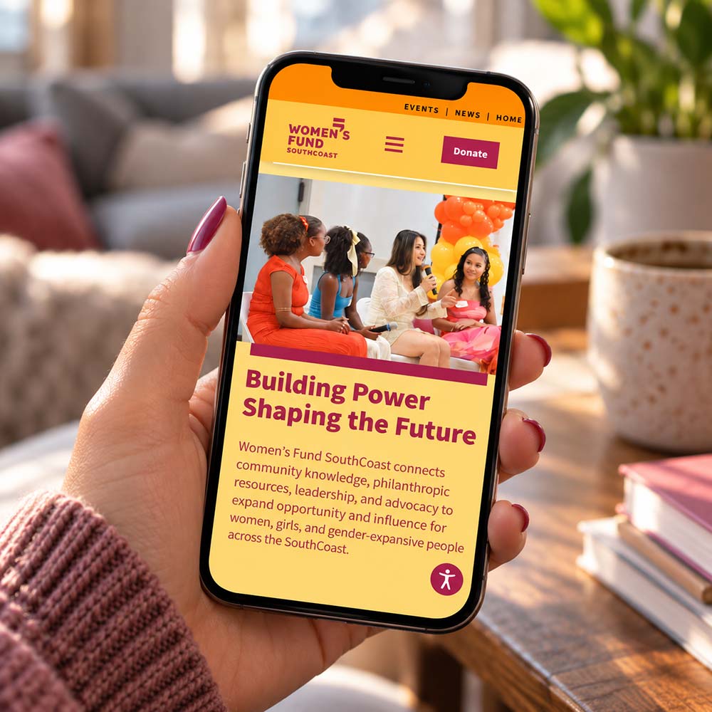 Women’s Fund SouthCoast website displayed on an iPhone in a home workspace.