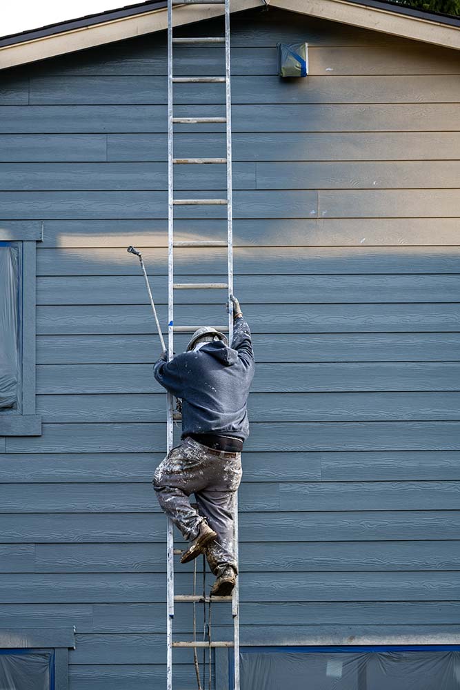 chm-home-services-painter-seo-4.jpg Professional painter climbing an extension ladder while painting residential siding.